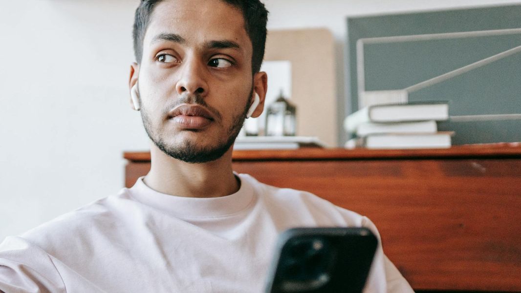 A person sitting at a desk with a laptop, a notebook, and a pen, looking thoughtful while listening to something on headphones.