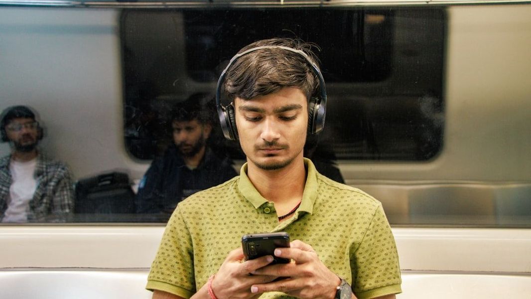 A person wearing noise-canceling headphones on a train, focused on learning from an audio article on their tablet.