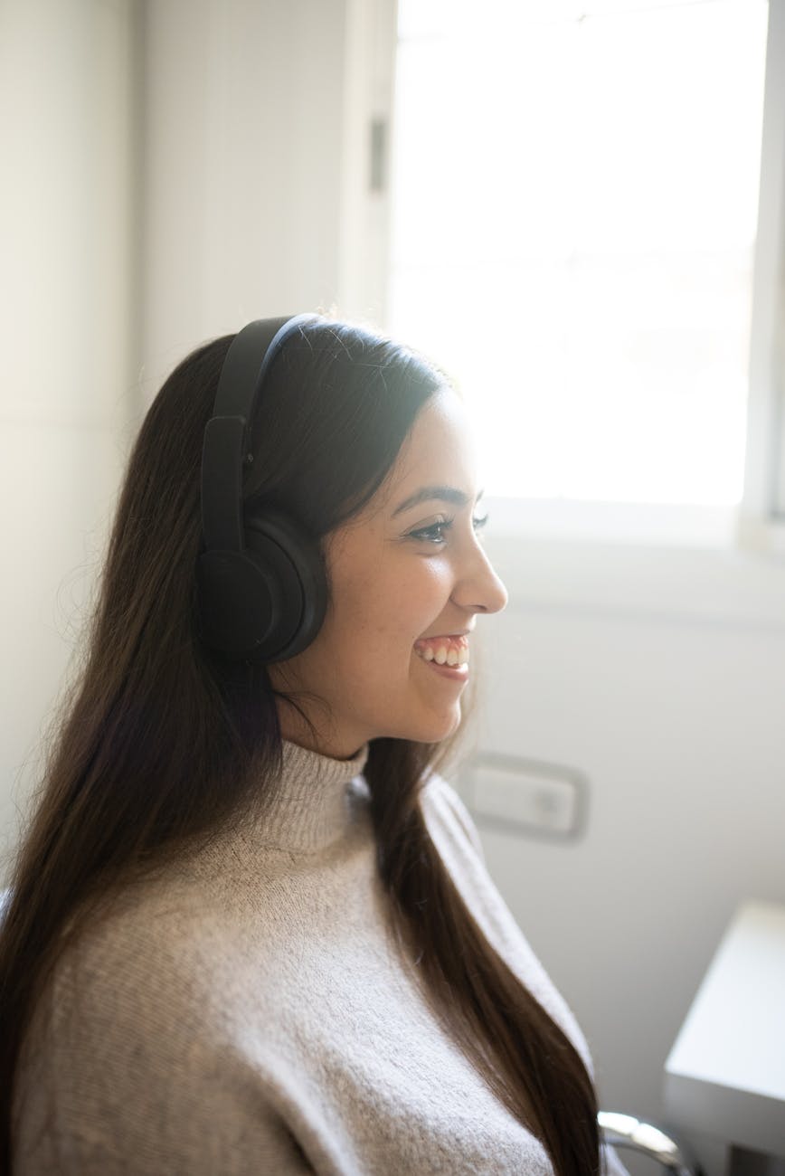 Side view of a woman wearing headphones and smiling indoors by a window.
