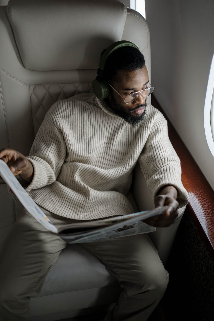 A man enjoying a quiet flight while reading a newspaper and listening to music with headphones.