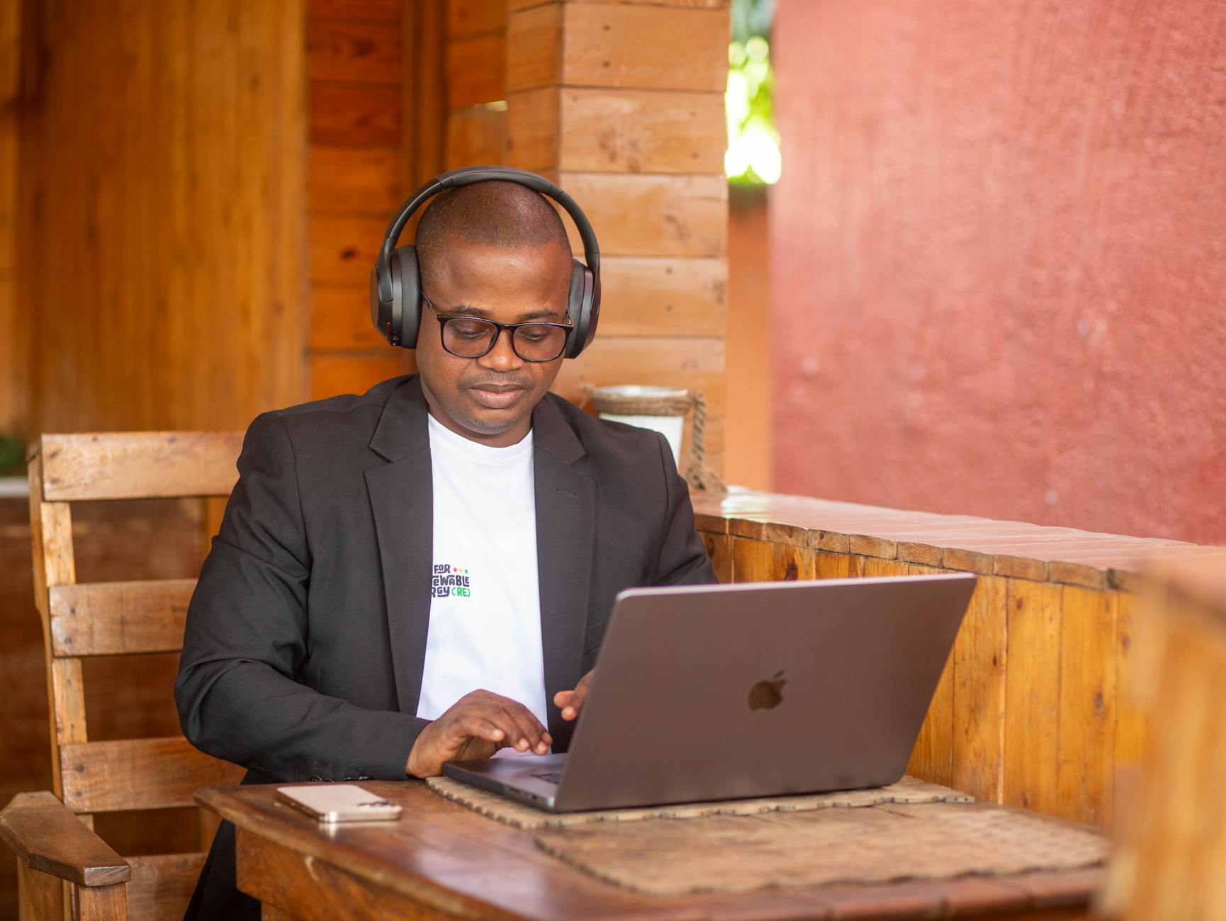 IMAGE: A person sitting at a desk with a laptop, open notebook, and headphones, looking focused and engaged