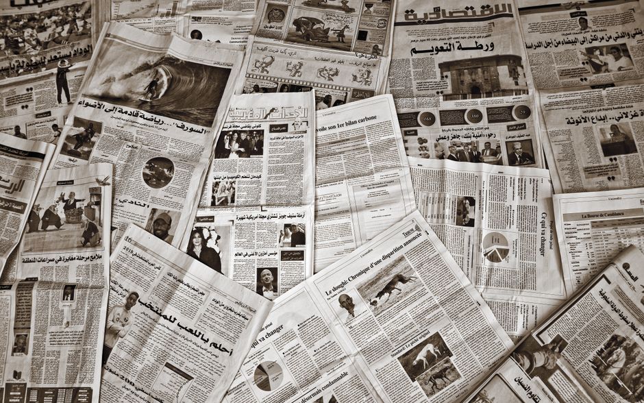 Arabic and French newspapers spread across a table, headlines overlapping